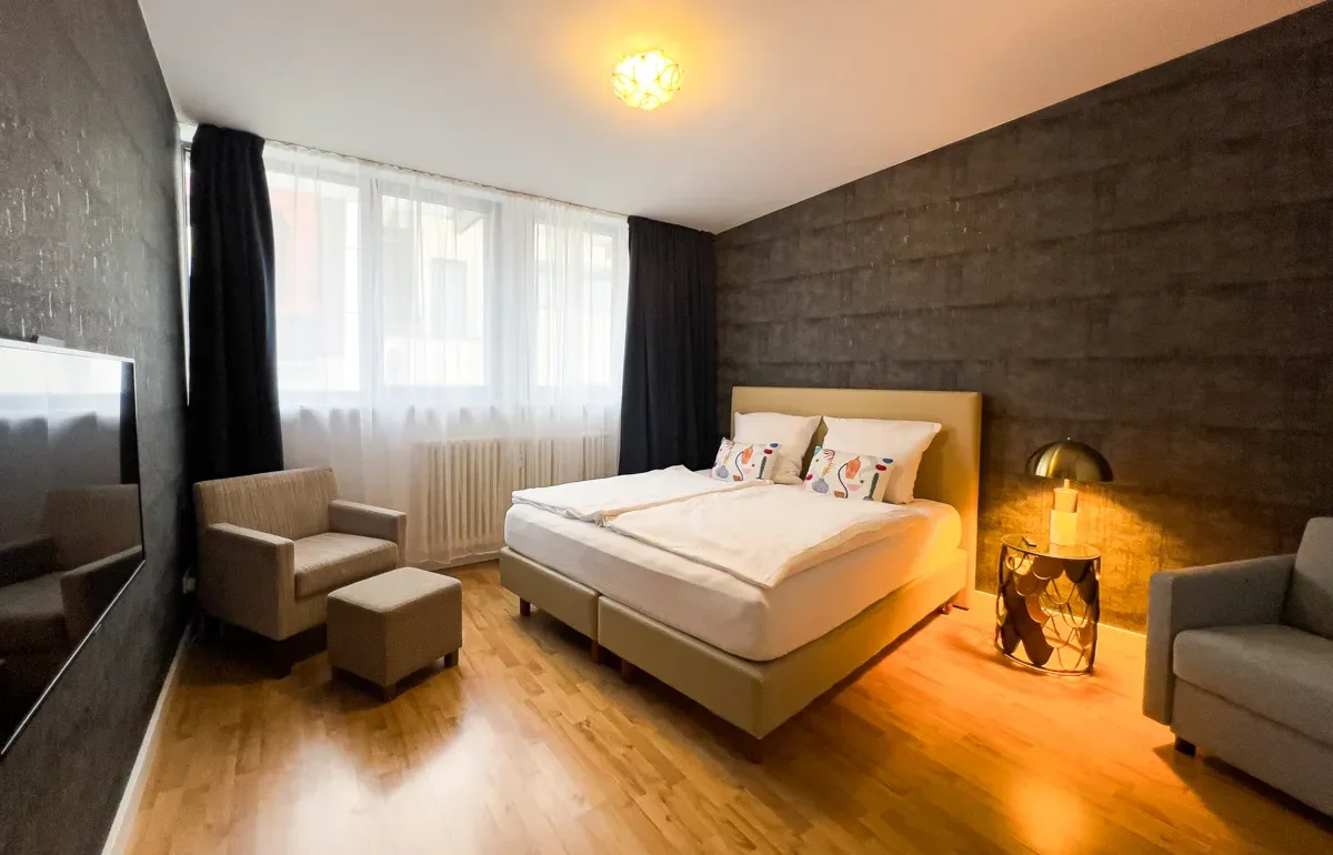 Schlafzimmer des Aurora Apartments in der Lodge Leipzig, ausgestattet mit Doppelbett und Sessel, spiegelt die einzigartige Themenwelt und Liebe zum Detail wider, die jeden Aufenthalt unvergesslich macht.