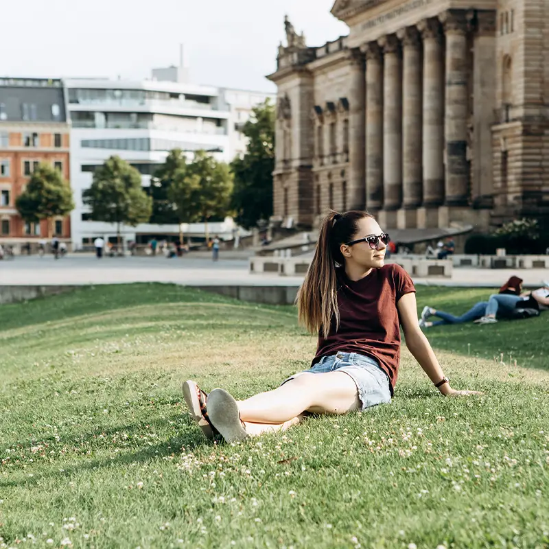 Frau sitzt auf einer Grünfläche in Leipzig, repräsentiert die Vielfalt der Gäste der Lodge Leipzig, von Geschäftsreisenden bis zu Kulturbegeisterten.