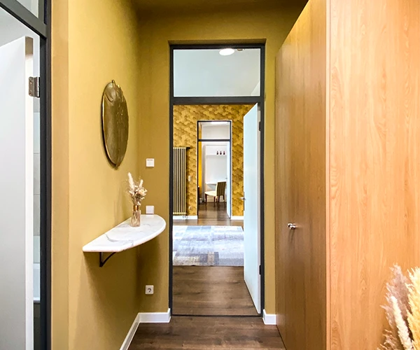 Ein heller, moderner Flur des Sunrise Apartments der Lodge Leipzig, ausgestattet mit einem glänzenden Holzboden und gold farbenen Wänden.