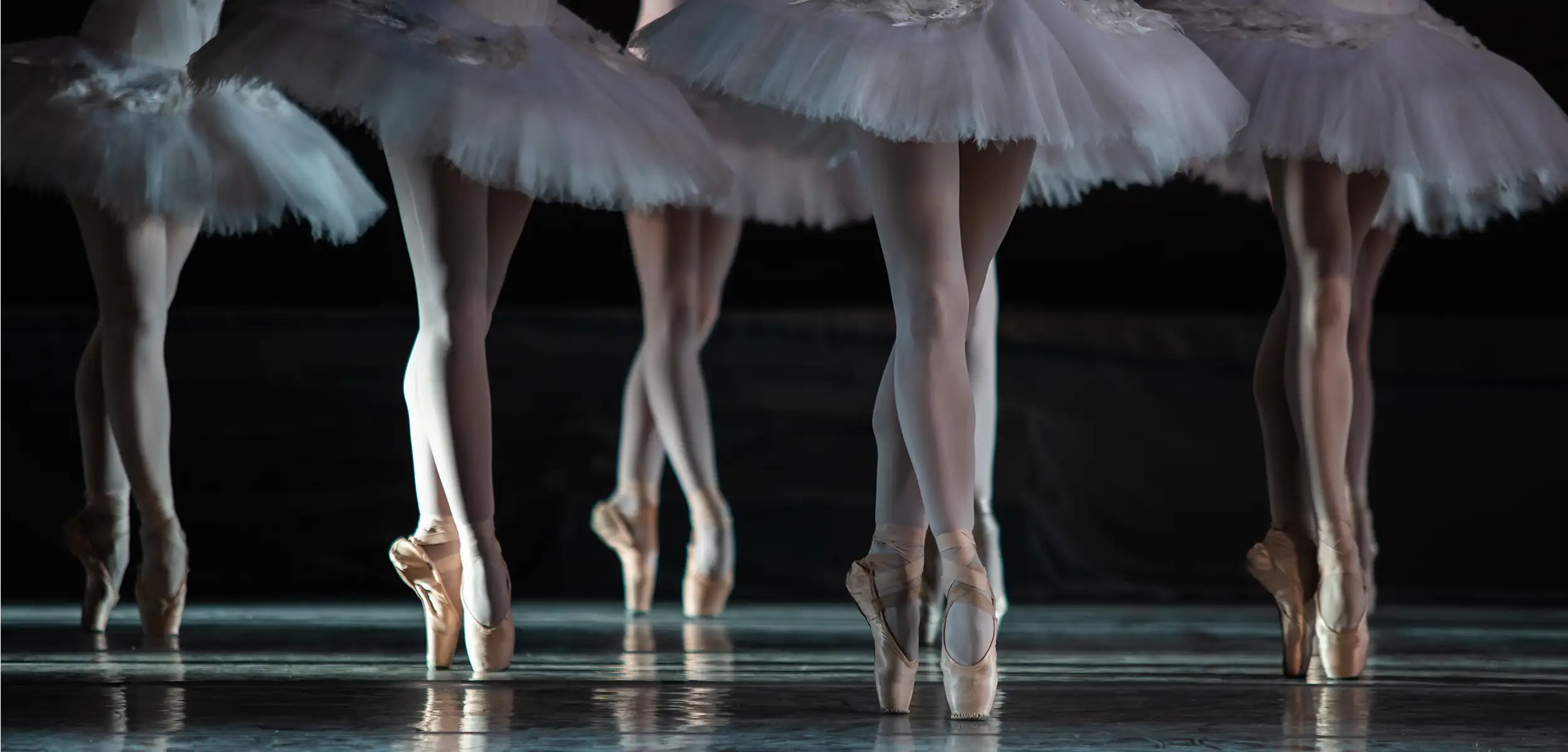 Balletttänzerin in einem weißen Tutu bei einer Aufführung von Schwanensee, in einer eleganten Pose auf der Bühne.