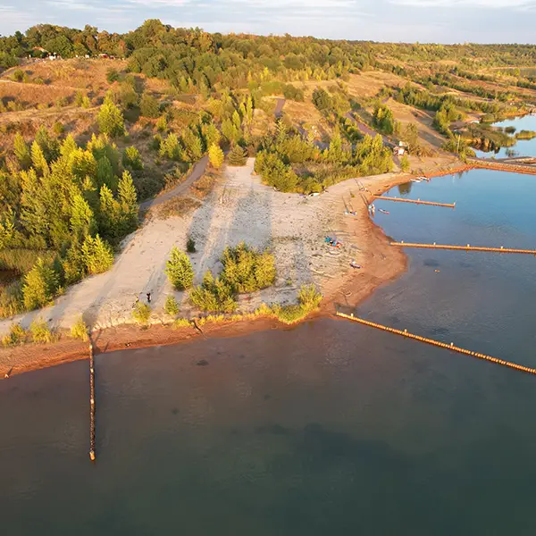 Sandstrand an einem See mit einem Baum in gelbem Herbstlaub am Ufer.