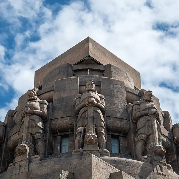 Nahaufnahme der steinernen Wächterfiguren am oberen Teil des Völkerschlachtdenkmals in Leipzig vor einem wolkigen Himmel.