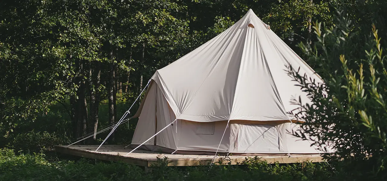 Ein großes, weißes Zelt steht auf einer Holzplattform, umgeben von Bäumen in einem Waldgebiet.