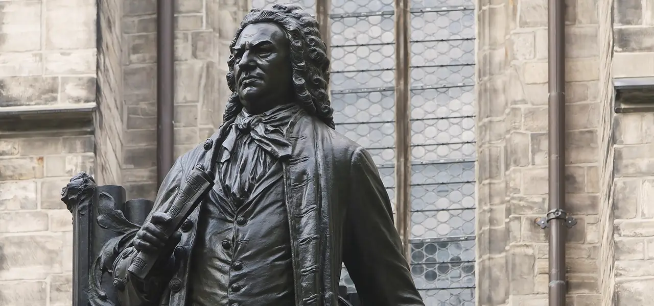 Statue eines Mannes in barocker Kleidung, der ein gerolltes Schriftstück in der Hand hält, vor einem Gebäude in Nähe des Bachmuseum Leipzig.