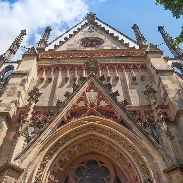 Außenansicht einer gotischen Kirche mit detaillierter Fassade, spitzen Türmen und einem großen Bogenportal, unter einem blauen Himmel.