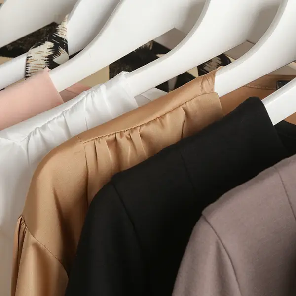 Mehrere Kleidungsstücke in neutralen Farben wie Beige, Weiß, Schwarz und Grau hängen ordentlich auf weißen Kleiderbügeln.
