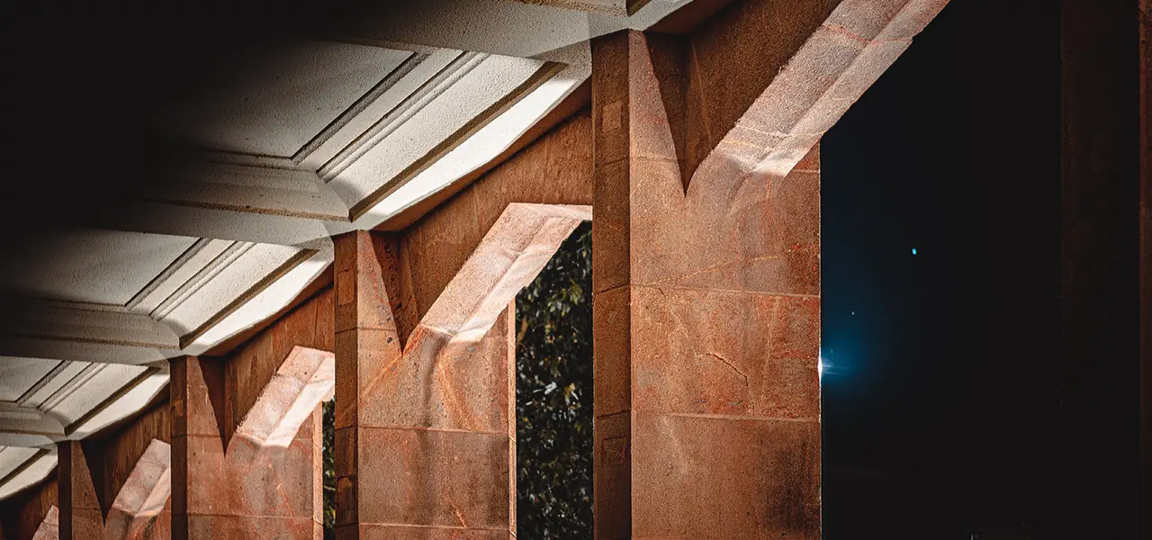 Nahaufnahme von Sandsteinbögen einer Arkade mit einfallendem Licht, das markante Schatten und Formen auf den Strukturen erzeugt.