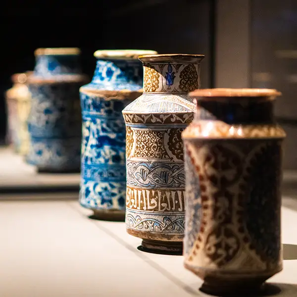 Eine Reihe kunstvoll verzierter Keramikgefäße mit arabischen Mustern und Schriftzügen, ausgestellt in einem Museum.