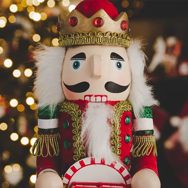 Nahaufnahme eines traditionellen Nussknackers in festlicher Kleidung mit Krone, vor einem unscharfen Hintergrund mit Lichterketten.