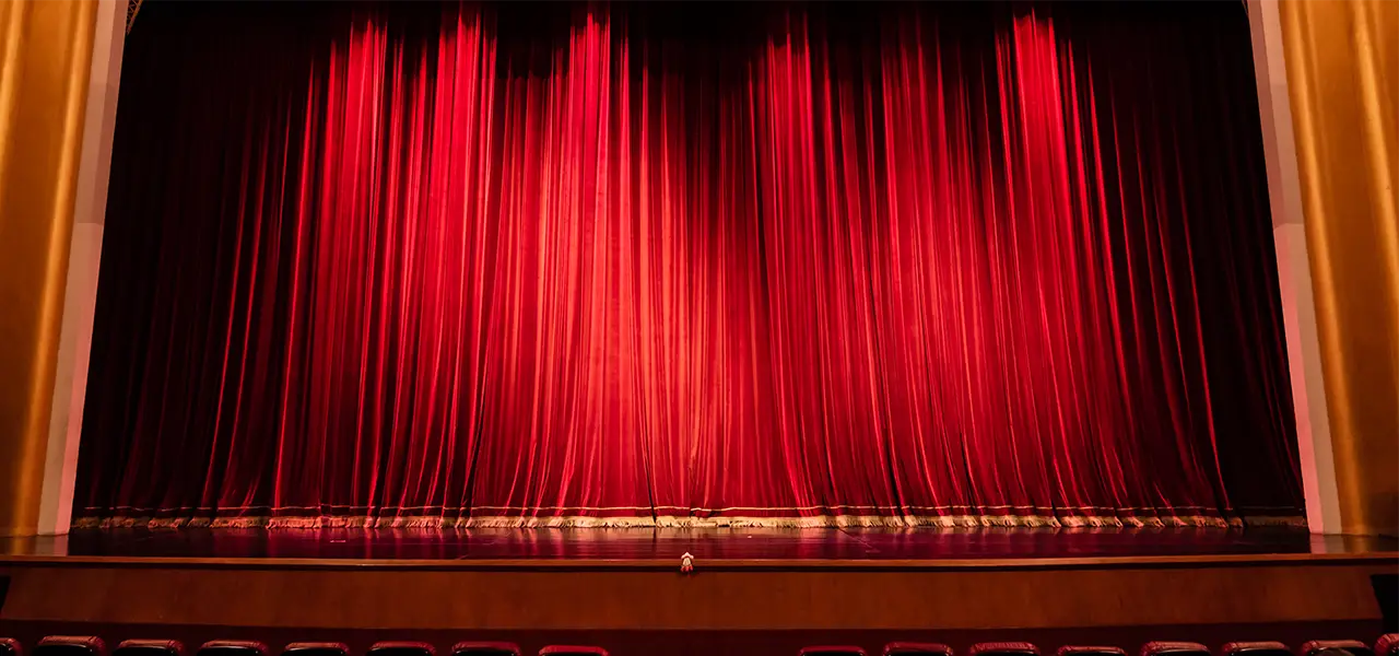 Geschlossene rote Samtvorhänge auf einer Theaterbühne der Musikalischen Komödie, umrahmt von goldenen Details.