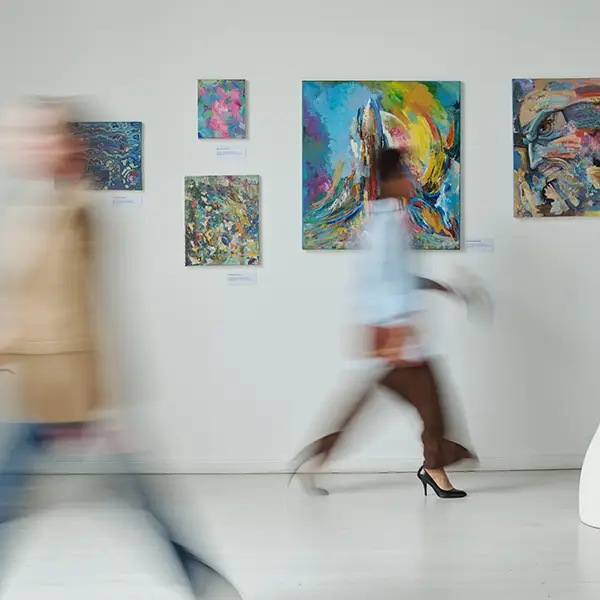 Kunstgalerie mit abstrakten Gemälden an einer weißen Wand, während unscharfe Personen vorbeigehen.